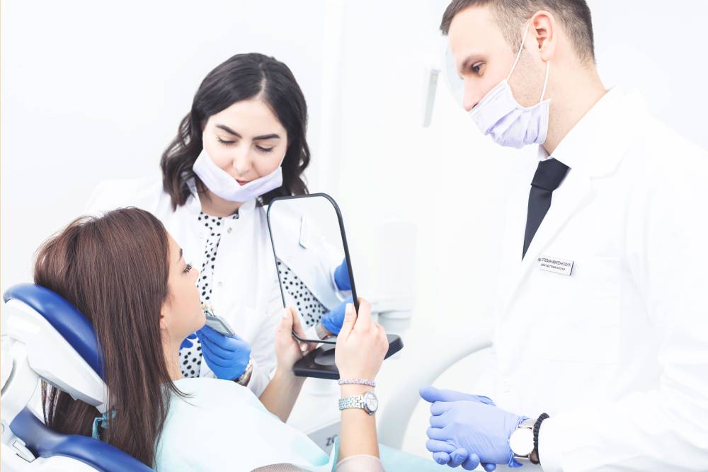 Slika zubara i tehničara sa pacijentom koja drži ogledalo